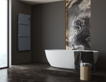 A sleek white freestanding bathtub and a dark grey vertical towel warmer accent this luxurious, modern bathroom featuring a backlit marble wall and dark herringbone floors.