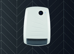 A sleek white wall-mounted electric fan heater displays a digital temperature of 23 degrees against a dark, chevron-patterned tiled wall.
